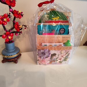 Sobre cargado lleno de cuaderno, máscaras de belleza, chocolates y objetos pequeños: regalo de Navidad para profesora, decoración floral rosa