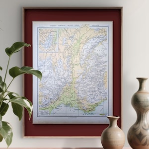 Könnte beinhalten: Gerahmter Vintage-Karten-Druck mit rotem Passepartout und hellem Holzrahmen. Die Karte zeigt eine detaillierte geografische Darstellung einer Region mit Text oben. Zwei dekorative Keramikvasen stehen auf einer roten Marmoroberfläche.