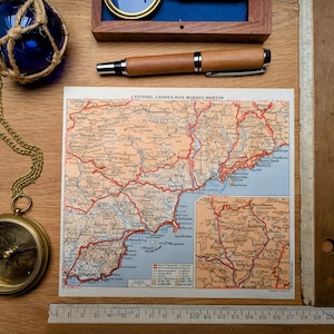 Peut inclure: Divers objets sur le thème du voyage et de la mer sur une surface en bois. Comprend une carte vintage, une boussole sur chaîne, un flotteur en verre bleu, un stylo en bois et une règle. La carte contient du texte en français.
