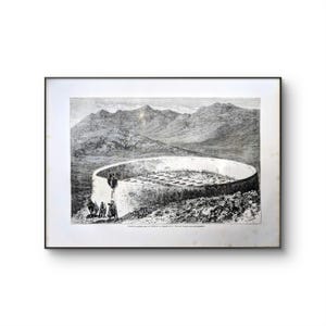 May include: A black and white framed print depicting a large circular stone structure situated in a mountainous landscape. The illustration shows figures near the base and a ladder leaning against the wall, with text printed at the bottom.