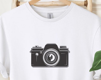May include: White t-shirt with a black and white illustration of a vintage camera.