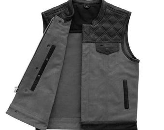 May include: A gray denim motorcycle vest with black leather accents. The vest has a quilted leather panel on the back and a zipper closure. The vest has a snap closure at the collar and two pockets on the front.