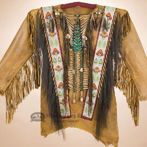 May include: A brown leather jacket with fringe and beaded trim. The jacket features a long, flowing fringe and a beaded design on the front. The jacket is decorated with feathers and beads.