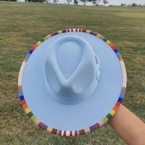 May include: A light blue fedora hat with a colorful beaded trim. The hat has a structured crown and a wide brim. The trim features a rainbow of colors, adding a vibrant accent to the hat's design.