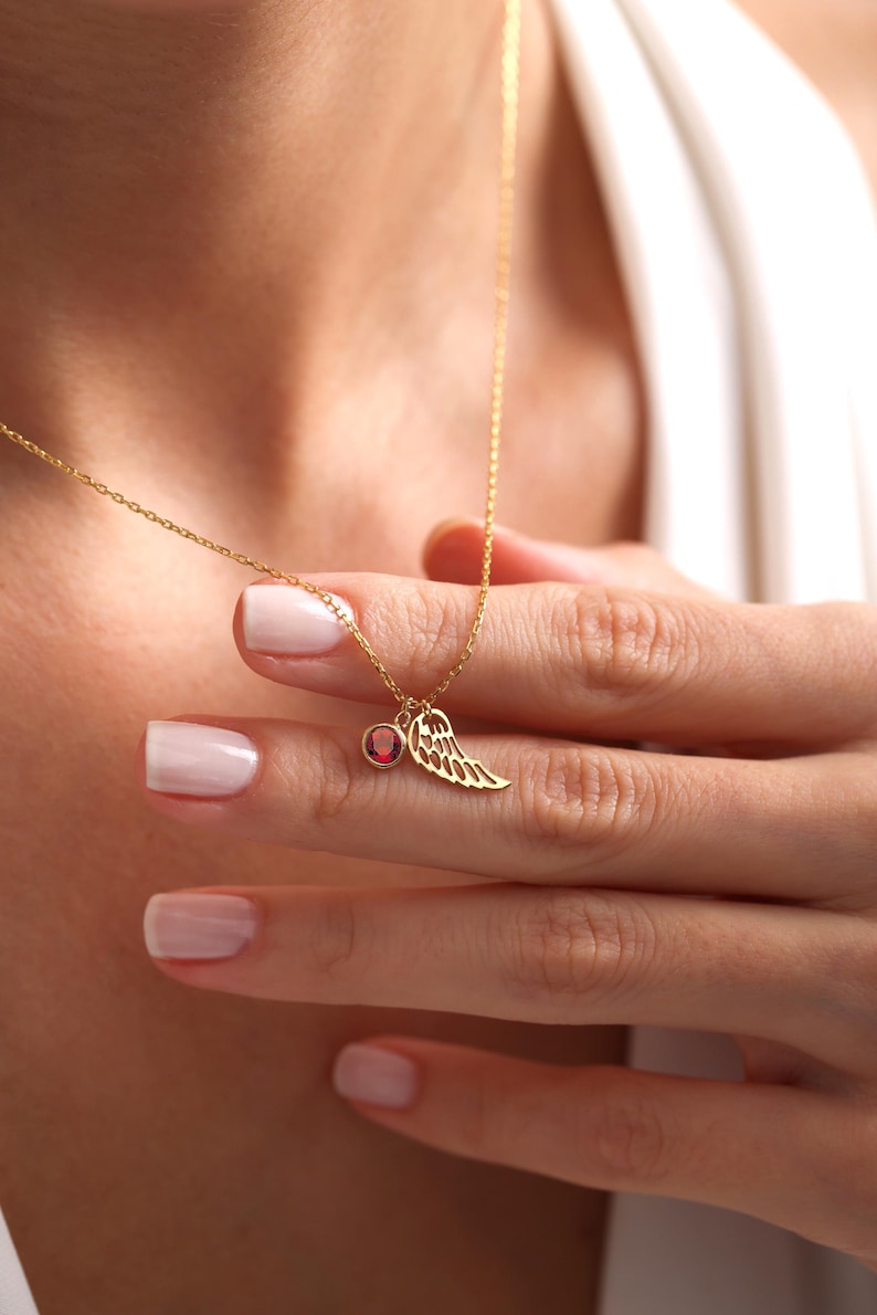 Op de afbeelding: Een gouden ketting met een klein rood edelsteentje en een delicate gouden vleugel hanger.