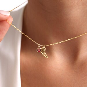 Op de afbeelding: Een gouden ketting met een klein rood edelsteentje en een delicaat gouden vleugelhangertje.