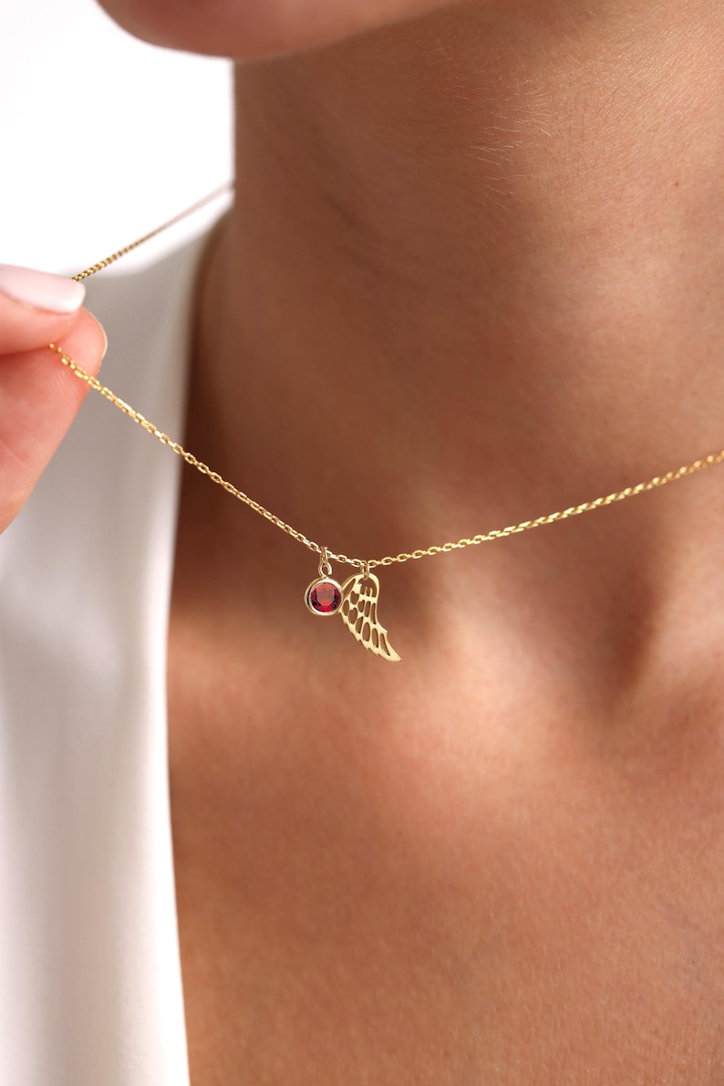 Op de afbeelding: Een gouden ketting met een klein rood edelsteentje en een delicaat gouden vleugelhangertje.