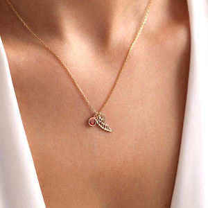 Op de afbeelding: Een gouden ketting met een kleine rode edelsteen en een delicate engelenvleugel hanger.