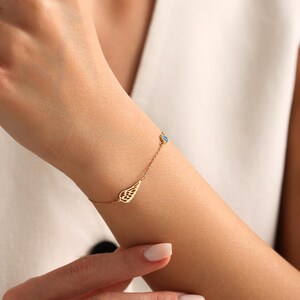 May include: A delicate gold bracelet featuring a wing charm and a small blue gemstone. The bracelet is worn on a wrist, showcasing its fine details and elegant design. The jewelry is a stylish accessory.