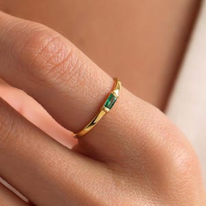May include: A gold ring with a single emerald green rectangular gemstone set in the centre.