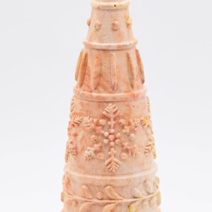 Puede incluir: Objeto decorativo en forma de cono de color naranja claro. Presenta intrincadas tallas de copos de nieve, hojas y patrones florales. El diseño recuerda a un árbol de Navidad o un adorno festivo.