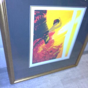 May include: Abstract art print in a gold frame. The artwork features a vibrant composition of red, yellow, and black hues. The framed art piece is displayed on a gray background, adding a touch of elegance to the overall presentation.