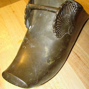 May include: A bronze, curved, decorative object with a floral design and a metal loop. The object has a smooth, worn surface.