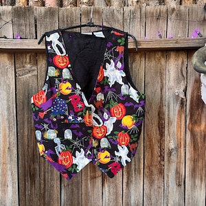May include: A black vest featuring a vibrant Halloween-themed print with orange jack-o'-lanterns, white ghosts, purple bats, spider webs, and tombstones. The sleeveless garment has a V-neckline, a button-front closure, and a solid black interior lining.