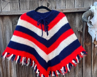 May include: A red, white, and blue striped crocheted poncho with fringe. The poncho has a tie at the neck.