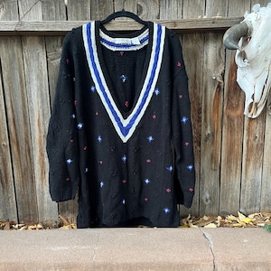 May include: Black knitted sweater with a white and blue v-neck trim and a small floral pattern.