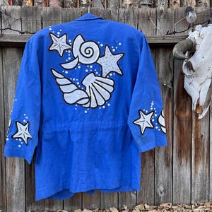 May include: A vibrant blue jacket adorned with white seashell and starfish designs. The jacket features a collared neckline, three-quarter sleeves, and a cinched waist. The back and sleeves are embellished with the sea-themed artwork.