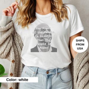 May include: White t-shirt with a black and white image of a person and the text "The Power of the People Is Greater Than The People In Power".