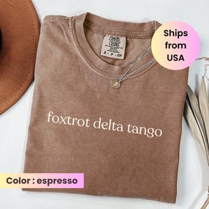 May include: Espresso-colored t-shirt with the text "foxtrot delta tango" in white. The shirt is a Comfort Colors brand and has a small silver necklace with a pendant. The shirt is a size small.