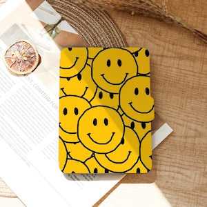May include: A yellow notebook cover with a repeating pattern of smiling faces. Each smiley face has black eyes and a curved black mouth. The background is a light yellow color. The notebook is rectangular.