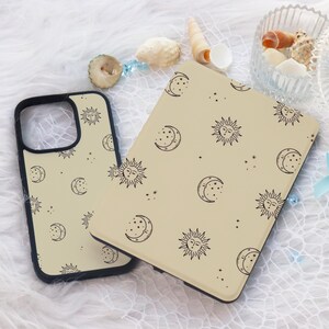 May include: Two beige phone cases with a black sun and moon pattern. The cases are made of a soft, flexible material and have a matte finish.