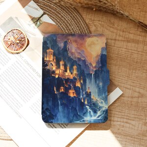 May include: A fantasy-themed tablet case featuring a vibrant painting of a castle nestled in a mountain range with waterfalls. The artwork showcases a warm, golden light illuminating the castle against a backdrop of blue and purple hues.