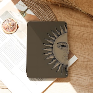 May include: A brown case featuring a detailed illustration of a sun with a face. The sun design is in a vintage style, with intricate lines and shading. The case is rectangular and appears to be for a tablet or e-reader.