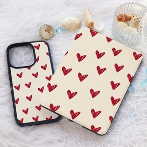 May include: A phone case and tablet case with a cream background and a pattern of red hearts. The phone case has a black border. The tablet case is open, revealing the interior.