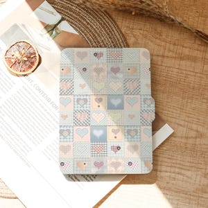 Peut inclure: Une housse de tablette aux couleurs pastel avec un motif patchwork représentant des cœurs dans divers motifs. L'étui a un fond bleu clair avec des carrés de différentes couleurs et textures. Le motif comprend des cœurs roses, bleus et verts.