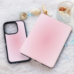 May include: Two pink phone cases with black edges are shown on a white, textured surface. One case is open, revealing the interior, while the other is closed. The cases are a soft pink colour.