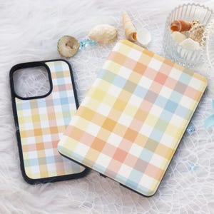 Può includere: Due custodie per telefono con un motivo a quadri colorati. Le custodie sono realizzate in materiale plastico rigido e hanno un bordo nero. Le custodie sono appoggiate su una superficie bianca e soffice.