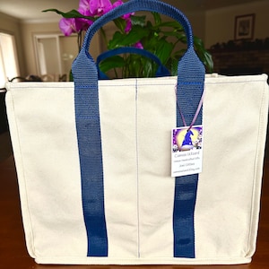 May include: A natural canvas tote bag with navy blue straps.