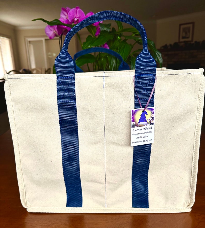 May include: A natural canvas tote bag with navy blue straps.