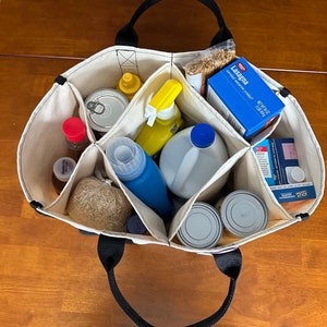 May include: A natural canvas tote bag with black handles and seven compartments.