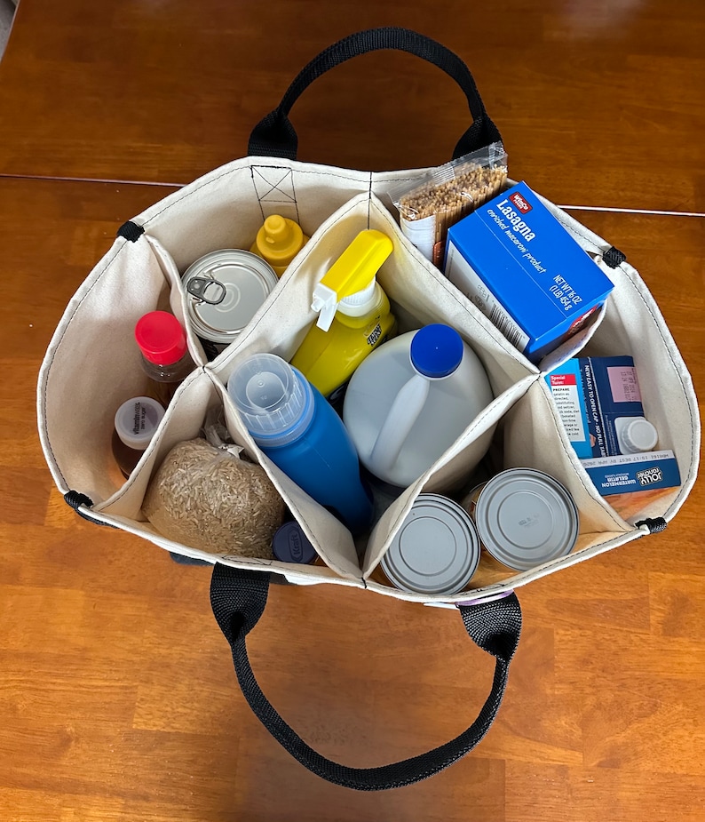 May include: A natural canvas tote bag with black handles and seven compartments.