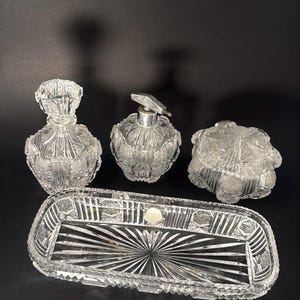 Könnte beinhalten: Ein durchsichtiges, geschliffenes Glas-Waschtisch-Set mit einer Parfümflasche, einer Sprühflasche, einem Deckelglas und einem rechteckigen Tablett. Das Set hat ein detailliertes, geometrisches Muster.