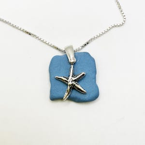 May include: A silver-toned starfish charm pendant attached to a flat, irregular, matte blue stone piece, suspended from a delicate silver-toned box chain necklace. The starfish features a textured, oxidized finish with five distinct arms.
