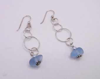 May include: A pair of silver dangle earrings with a light blue glass bead at the bottom of each earring. The earrings feature a chain of connected silver rings.