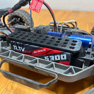 May include: Close-up of a black and red 11.1V 5300 mAh battery pack inside a gray and black remote control car. The battery is labeled "WE POWER". The car has black tires and a blue motor.
