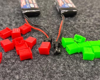 Op de afbeelding: Een close-up van twee sets elektrische connectoren. De ene set is rood en de andere is groen. De connectoren bevinden zich op een grijs oppervlak.