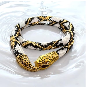 Op de afbeelding: Een kralen slangenketting met een goud en zwart patroon. De ketting heeft een gouden slangenkop sluiting.