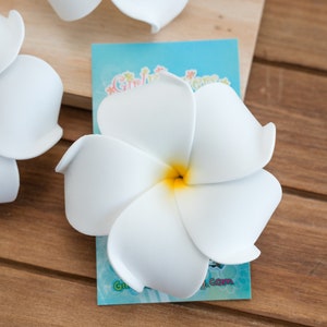 May include: White plumeria flower with a yellow center. The flower is made of foam and is a popular Hawaiian lei decoration.