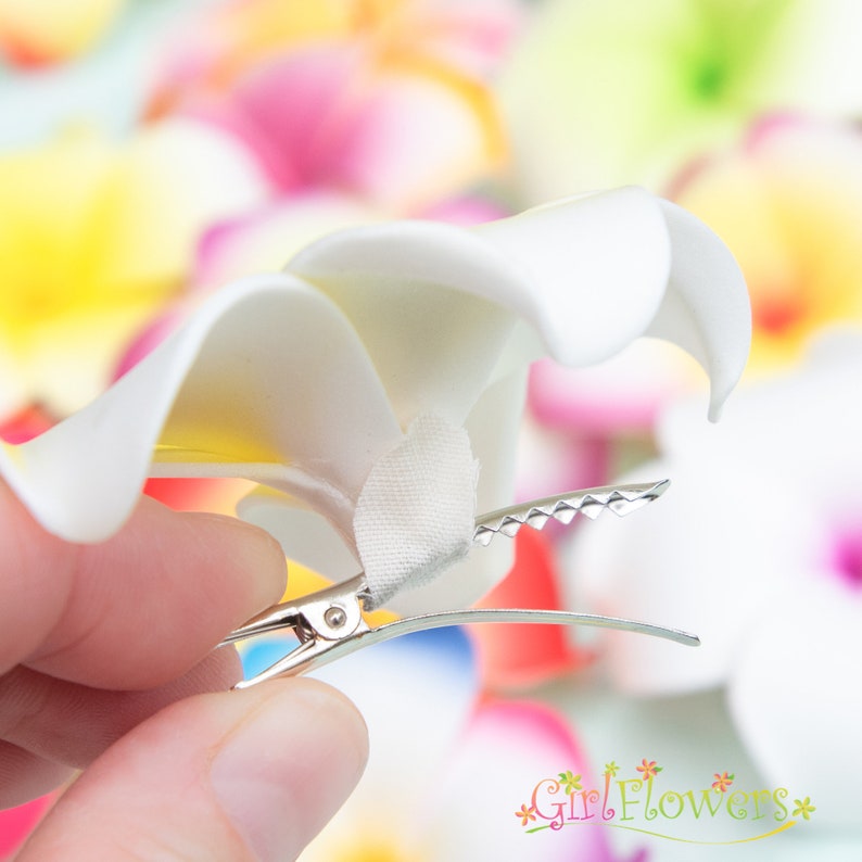 May include: White flower hair clip with a silver clip. The flower is made of fabric and has a layered design.