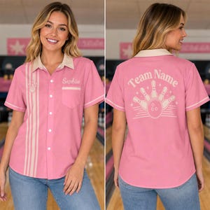 May include: A pink short-sleeved button-down bowling shirt with a cream-coloured collar and vertical stripes on the front. The front features the name Sophia, while the back displays a graphic of bowling pins and a ball with the text Team Name.