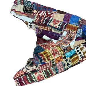 Op de afbeelding: Een patchwork sjaal met diverse geometrische en tribale patronen in rood, blauw, groen en beige tinten. De sjaal heeft een trekkoordsluiting en is gemaakt van een zachte, lichte stof.