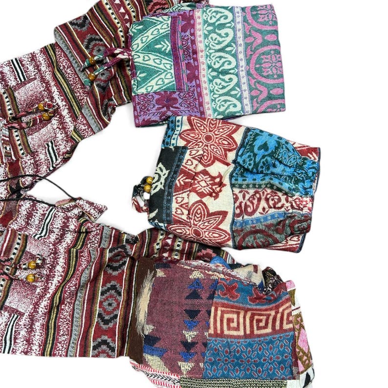 K&ouml;nnte beinhalten: Sortiment an farbenfrohen Stoffbeuteln mit Mustern. Die Beutel weisen eine Vielzahl von Designs auf, darunter Streifen, Blumenmuster und geometrische Formen. Jeder Beutel hat einen Kordelzugverschluss mit Holzperlen. Die Farbpalette umfasst Rot, Blau, Gr&uuml;n und Lila.