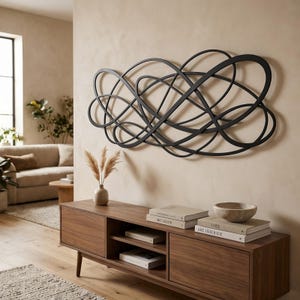 May include: A large, black, horizontal wall sculpture featuring an abstract design of interconnected, flowing loops and curved lines. The piece is constructed from thin, flat metal strips that create a continuous, complex, and overlapping pattern.