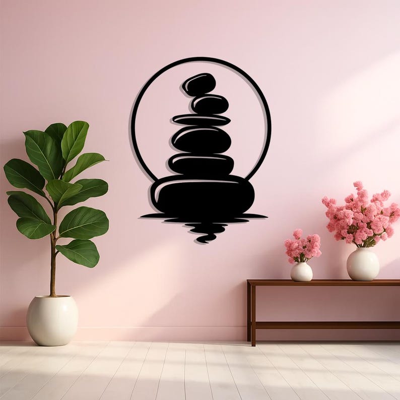 May include: Black metal wall art depicting a stack of smooth stones within a circle, symbolizing balance and serenity. The artwork is mounted on a light pink wall, creating a minimalist and zen-like aesthetic. The design includes a reflection effect.