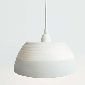 May include: White ceramic pendant light with a light blue glaze on the bottom half of the shade.