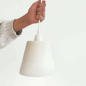 May include: White ceramic pendant light with a ribbed texture. The light is hanging from a white cord.